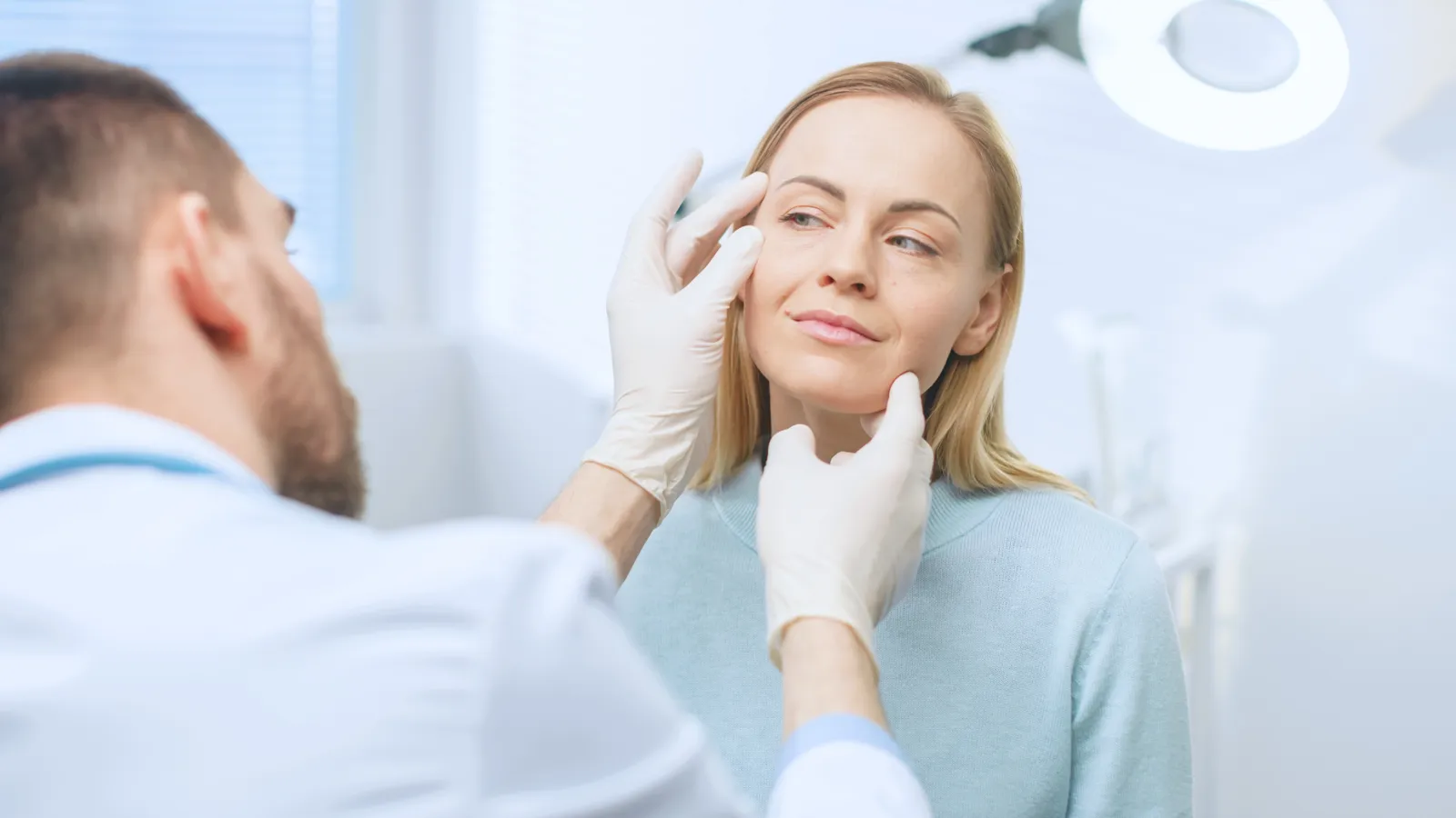 Surgeon examines a woman's cheeks with gloved hands